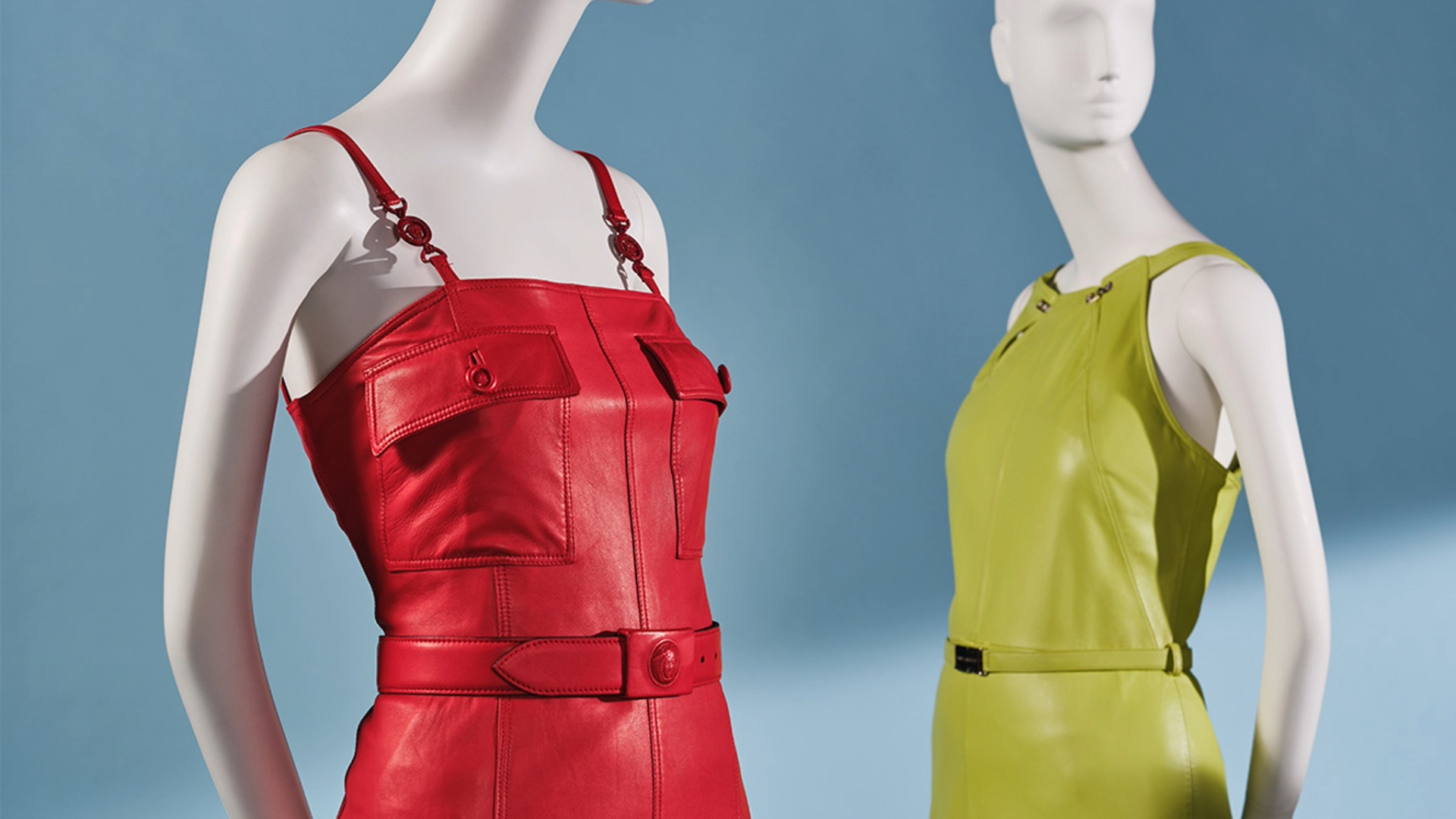Two mannequins, one with red leather dress and the other with a green leather dress